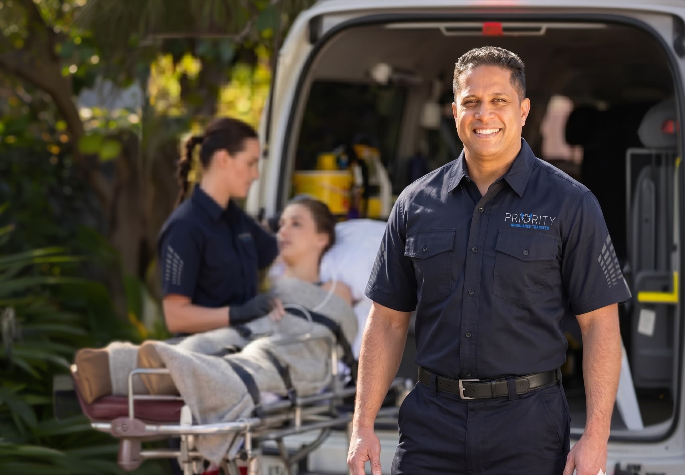 A Priority Ambulance Transfer paramedic standing beside an ambulance, smiling at the camera.